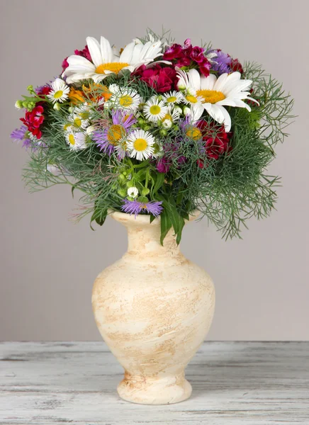 Mooie heldere bloemen in vaas op tafel op grijze achtergrond — Stockfoto