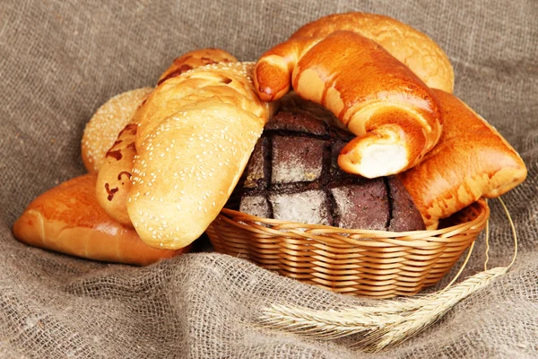 Baked bread in wicker basket on burlap background — Stockfoto