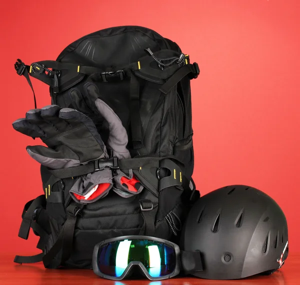 Wintersportbrille, Helm und Handschuhe, Rucksack, auf rotem Hintergrund — Stockfoto