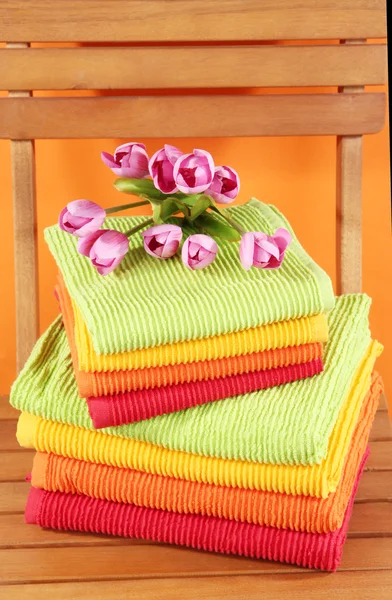 Ręczniki i kwiaty na drewniane krzesło na pomarańczowym tle — Zdjęcie stockowe