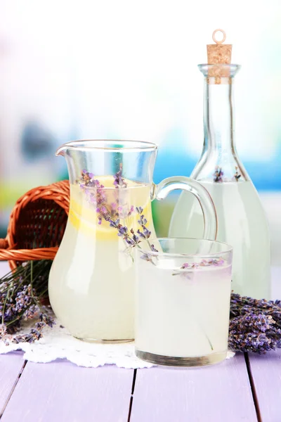 Lavender lemonade in glass bottle and jug, on violet wooden table, on bright background — Stock Photo, Image