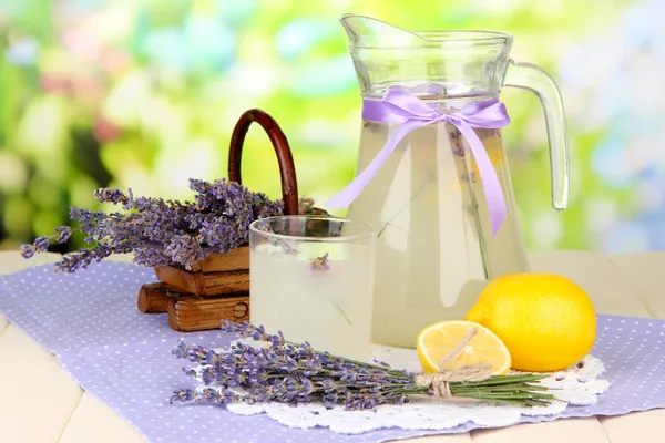 Lavender lemonade in glass jug and cocktail glasses, on bright background
