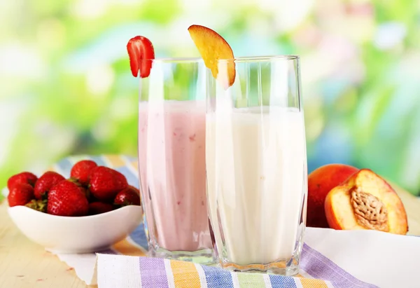 Leckere Milchshakes mit Erdbeeren und Pfirsich auf Holztisch vor natürlichem Hintergrund — Stockfoto