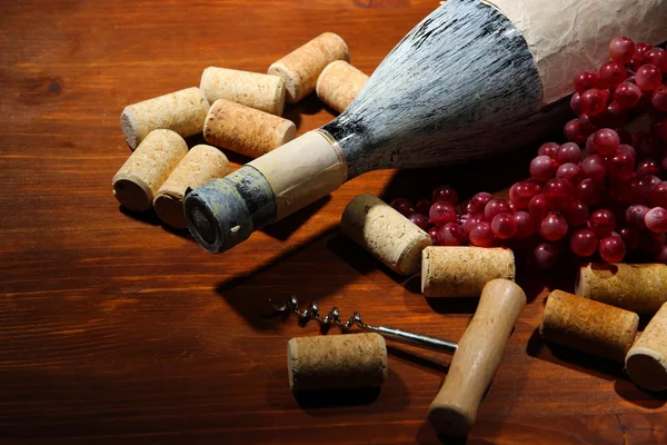 Stará láhev vína, vinných hroznů a zátky na dřevěné pozadí — Stock fotografie