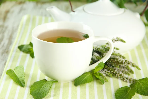Bule e xícara de chá de ervas com flores frescas de hortelã na mesa de madeira — Fotografia de Stock