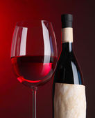 Sklenka vína s lahví na zářivě červeném pozadí