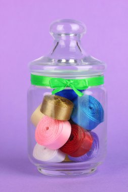 Lila zemin üzerine çeşitli renkli kurdeleler içeren Cam Kavanoz