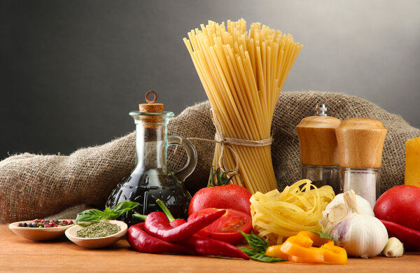 Pasta spaghetti, vegetables and spices, on wooden table, on grey background