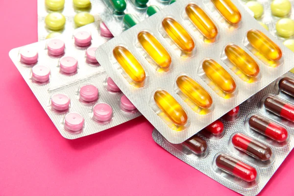 Cápsulas y pastillas empaquetadas en ampollas, sobre fondo rosa —  Fotos de Stock