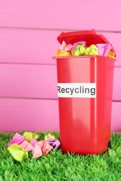Papelera de reciclaje con papeles sobre hierba sobre fondo rosa —  Fotos de Stock