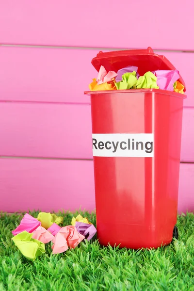 Recycling bin with papers on grass on pink background — Stock Photo, Image