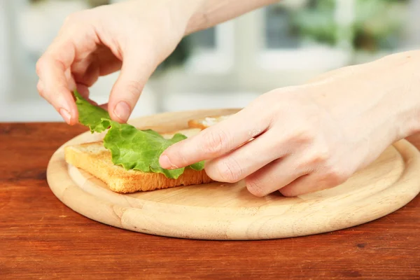 Διαδικασία εκπόνησης σαλάμι ρολά στο ψητό ψωμί, σε φωτεινό φόντο: γυναικείο χέρι βάζει φύλλα σαλάτα με ψητό ψωμί — Φωτογραφία Αρχείου