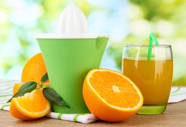 Citrus press, glass of juice and ripe oranges on brown wooden table — Stock Photo, Image