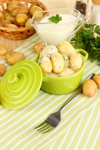 Tender young potatoes with sour cream and herbs in pan on wooden table close-up — Stock Photo, Image