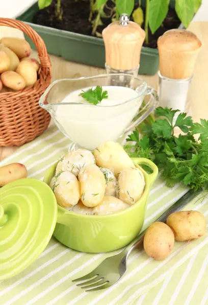 Inschrijving van jonge aardappelen met zure room en kruiden in pan op houten tafel close-up — Stockfoto