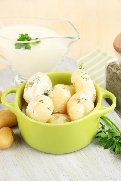 Jeunes pommes de terre tendres à la crème sure et aux herbes dans une casserole sur une planche de bois sur une table close-up — Photo