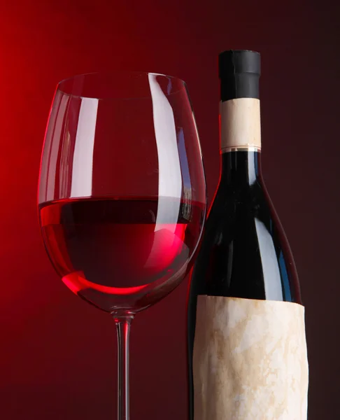 Bicchiere di vino con bottiglia su sfondo rosso brillante — Foto Stock