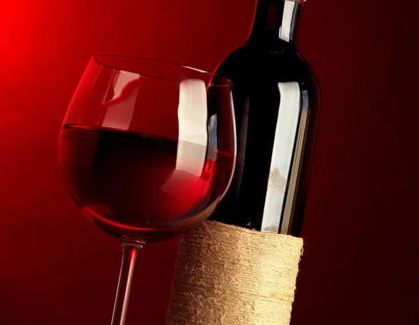 Bicchiere di vino con bottiglia su sfondo rosso brillante — Foto Stock