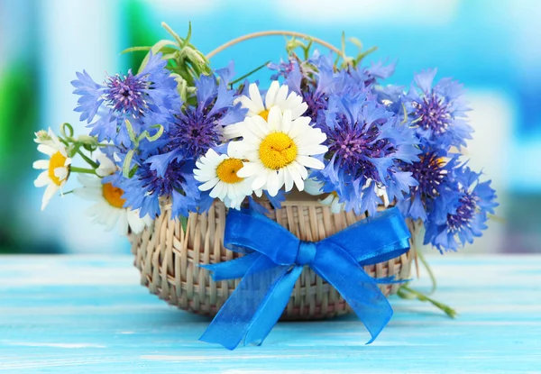 Beautiful bouquet of cornflowers and chamomiles in basket on blue background — Stock Photo, Image