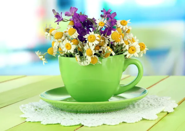 Bouquet of chamomile flowers in cup, on bright background — Stock Photo, Image