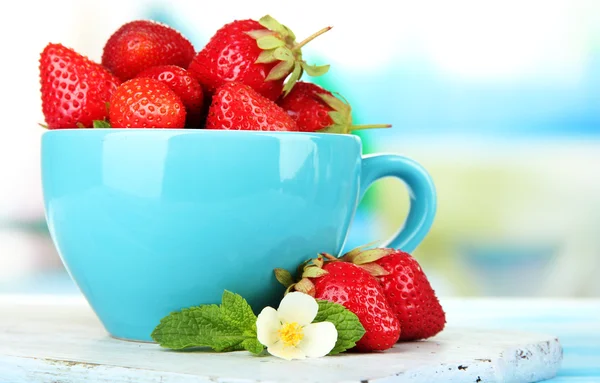 Fresas dulces maduras en taza sobre mesa de madera azul —  Fotos de Stock