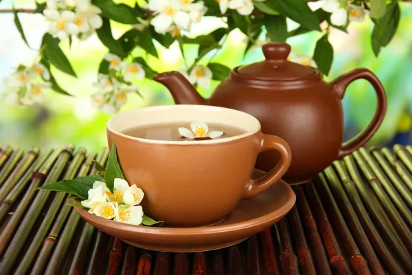 Cup of tea with jasmine, on bamboo mat, on bright background — Stock Photo, Image