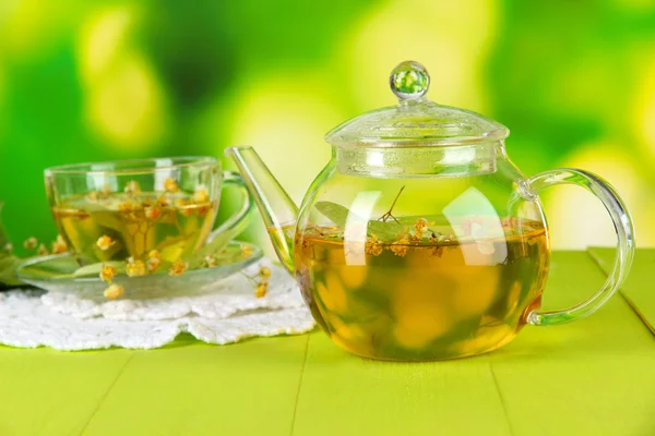 Чайник и чашка чая с липой на деревянном столе на природе — стоковое фото