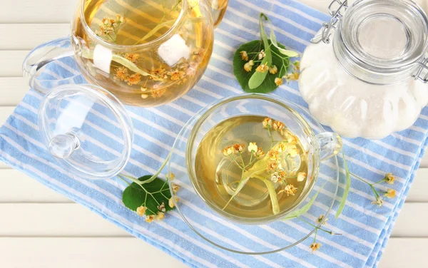 Hervidor de agua y taza de té con tilo en servilleta sobre mesa de madera —  Fotos de Stock