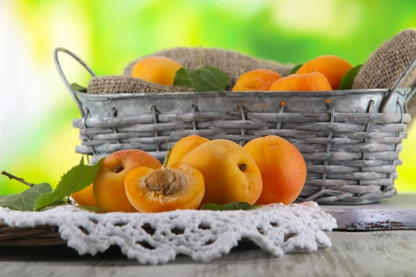 Apricots in basket on napkin on wooden table on nature background — Stock Photo, Image