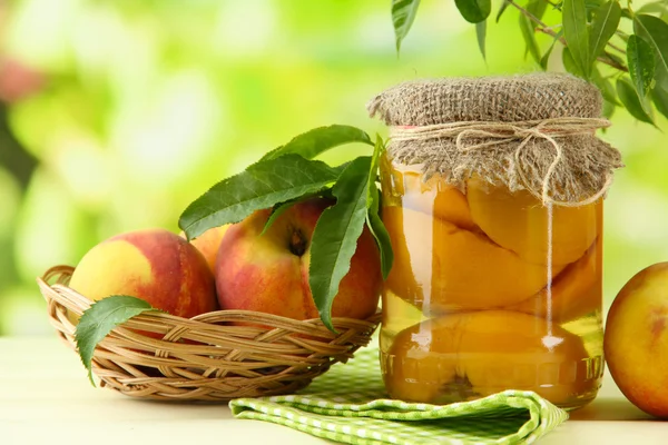 Jar of canned peaches and fresh peaches on wooden table, outside