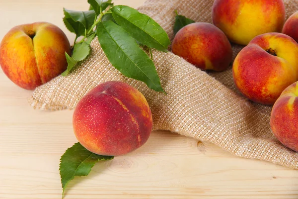 Peaches on sackcloth on wooden table — Stock Photo, Image