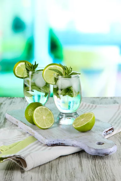 Glasses of cocktail with ice on board on napkin on wooden table on room background — Stock Photo, Image