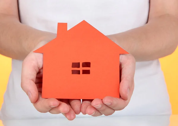 Papier huis in handen op oranje achtergrond — Stockfoto
