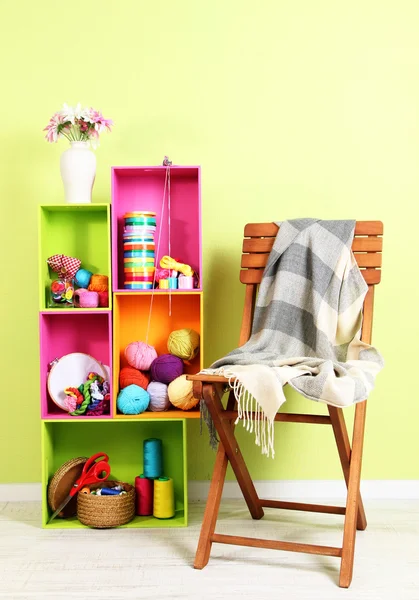 Colorful shelves of different colors with utensils near chair with plaid on wall background — Stock Photo, Image