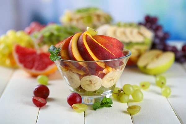 Salada de frutas saborosas em tigela de vidro, na mesa de madeira branca — Fotografia de Stock