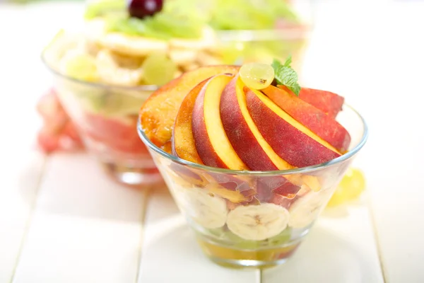 Salade de fruits savoureuse dans des bols en verre, sur une table en bois blanc — Photo