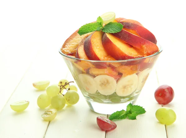 Salada de frutas saborosas em tigela de vidro, na mesa de madeira branca — Fotografia de Stock