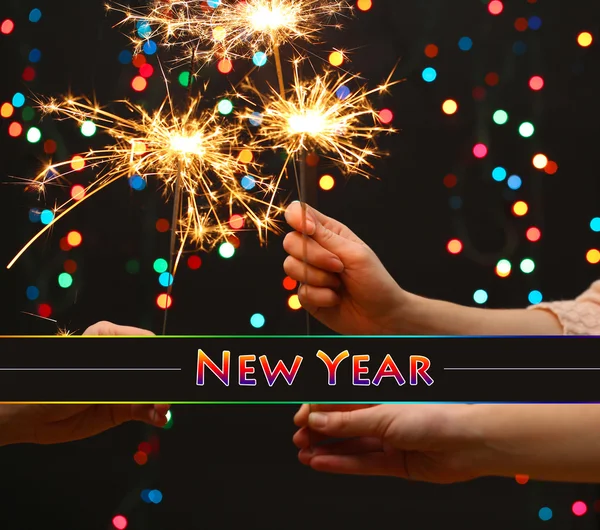 Beautiful sparklers in woman hands on garland background — Stock Photo, Image