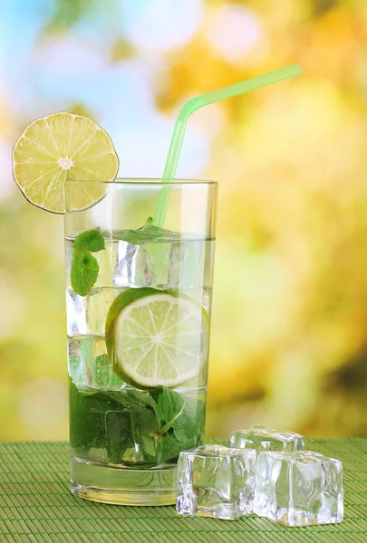 Bicchiere d'acqua con ghiaccio, menta e calce sul tavolo su sfondo luminoso — Foto Stock