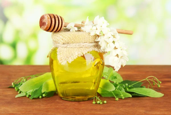 Jar of honey with flowers of lime, acacia on wooden table on bright background — Stock Photo, Image