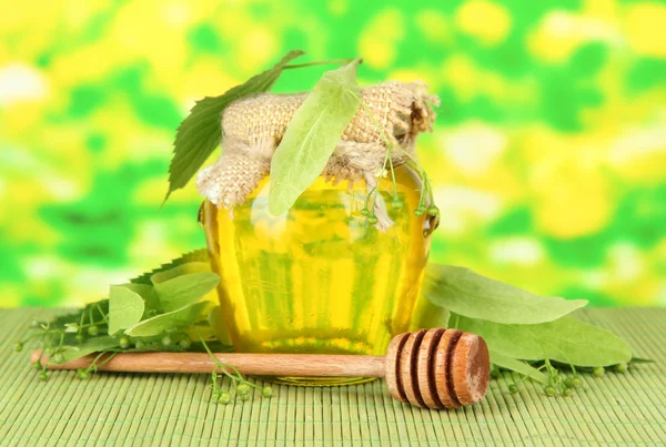 Jar of honey with flowers of lime, on color bamboo mat on bright background — Stock Photo, Image