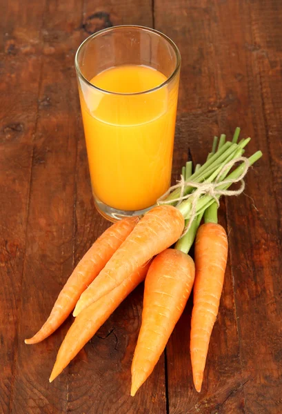 Un mucchio di carote, vetro di succo, su sfondo di legno — Foto Stock