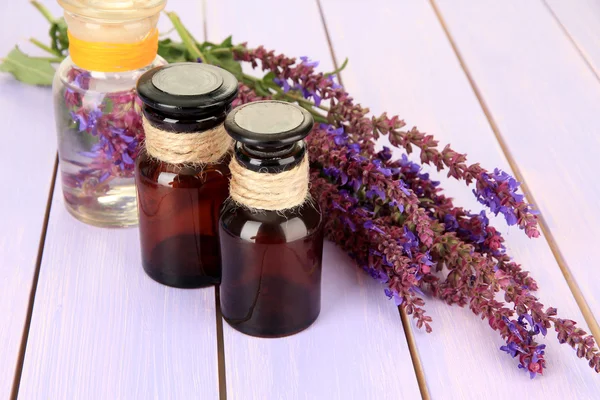 Geneeskundeflessen en salvia bloemen op paarse houten achtergrond — Stockfoto