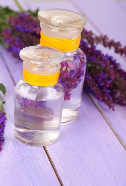 Geneeskundeflessen met salvia bloemen op paarse houten achtergrond — Stockfoto