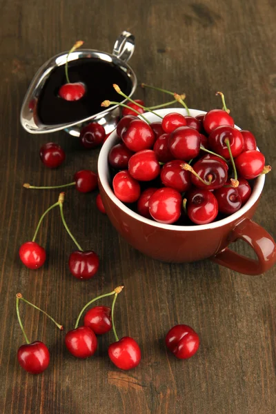 Bayas rojas maduras de cereza en taza y salsa de chocolate en primer plano de mesa de madera — Foto de Stock