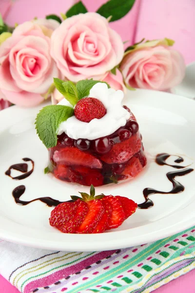 Finom zselés desszert a friss bogyós gyümölcsök, rózsaszín rózsa háttér — Stock Fotó