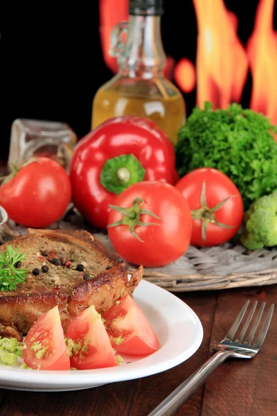 Stekt köttbit på plattan på träbord på brand bakgrund — Stockfoto