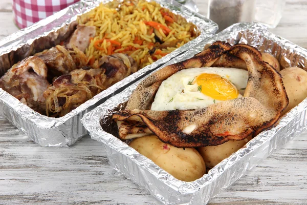 Food in boxes of foil on wooden table — Stock Photo, Image