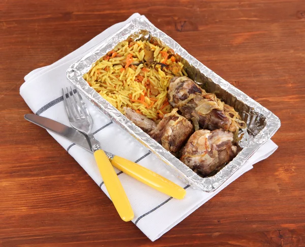 Еда в коробке фольги на салфетке на деревянном фоне — стоковое фото
