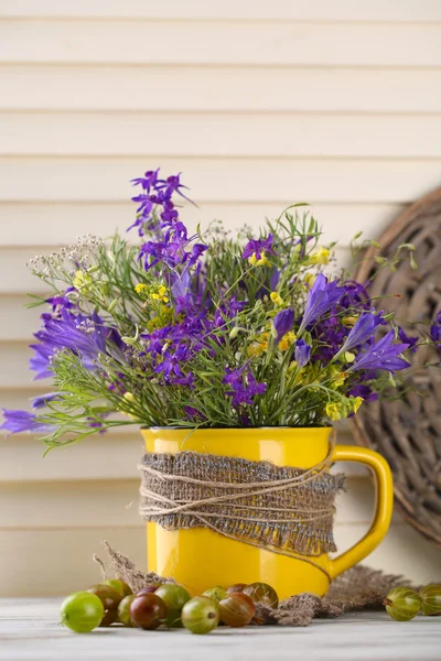 Beautiful bouquet of wildflowers in cup and berries on wooden table — Stock Photo, Image